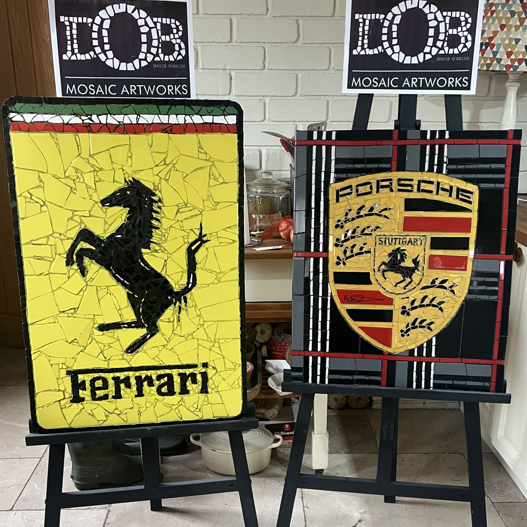 Two handcrafted ceramic mosaic wall artworks featuring Ferrari and Porsche badges, created as bespoke commissions. Each piece is made from hand-cut ceramic tiles in yellow, red, black, white, and grey, celebrating classic motorsport design and automotive heritage through contemporary mosaic craftsmanship.