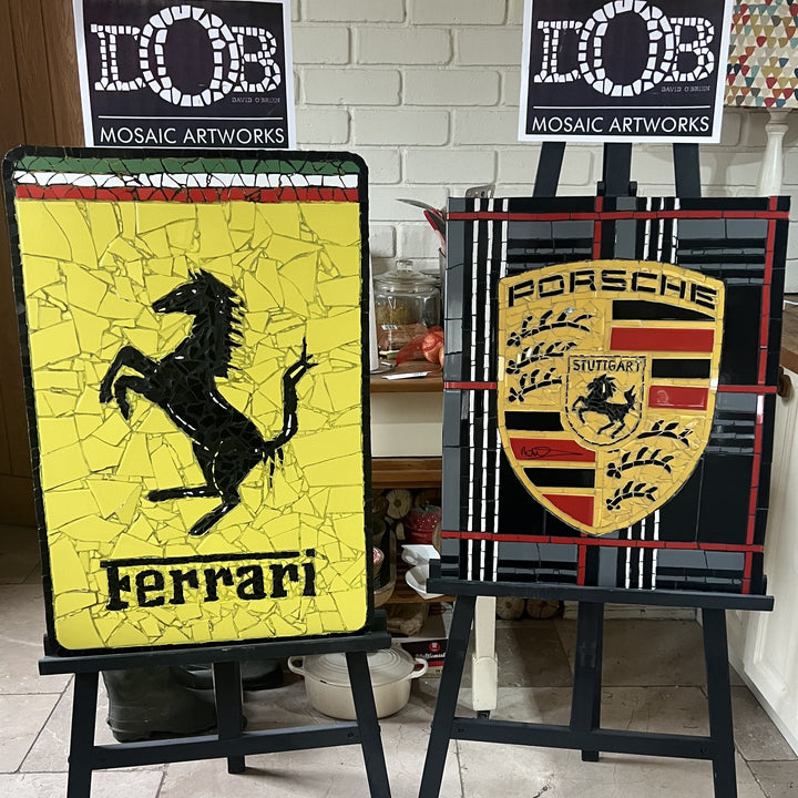 Two handcrafted ceramic mosaic wall artworks featuring Ferrari and Porsche badges, created as bespoke commissions. Each piece is made from hand-cut ceramic tiles in yellow, red, black, white, and grey, celebrating classic motorsport design and automotive heritage through contemporary mosaic craftsmanship.