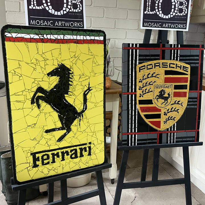 Two handcrafted ceramic mosaic wall artworks featuring Ferrari and Porsche badges, created as bespoke commissions. Each piece is made from hand-cut ceramic tiles in yellow, red, black, white, and grey, celebrating classic motorsport design and automotive heritage through contemporary mosaic craftsmanship.