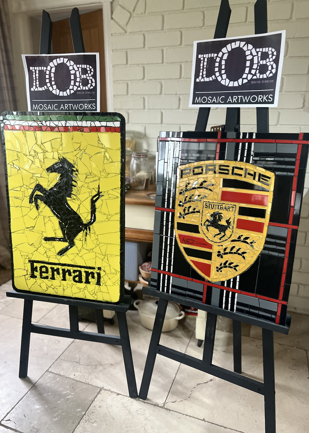Two handcrafted ceramic mosaic wall artworks featuring Ferrari and Porsche badges, created as bespoke commissions. Each piece is made from hand-cut ceramic tiles in yellow, red, black, white, and grey, celebrating classic motorsport design and automotive heritage through contemporary mosaic craftsmanship.