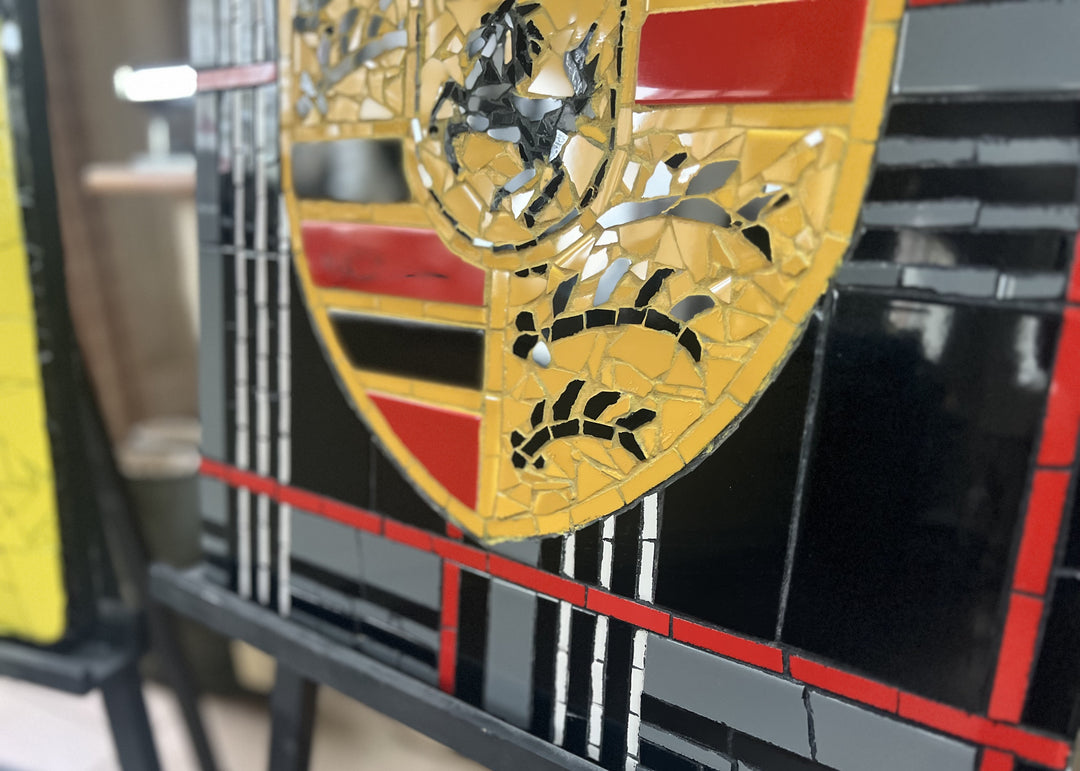 Two handcrafted ceramic mosaic wall artworks featuring Ferrari and Porsche badges, created as bespoke commissions. Each piece is made from hand-cut ceramic tiles in yellow, red, black, white, and grey, celebrating classic motorsport design and automotive heritage through contemporary mosaic craftsmanship.