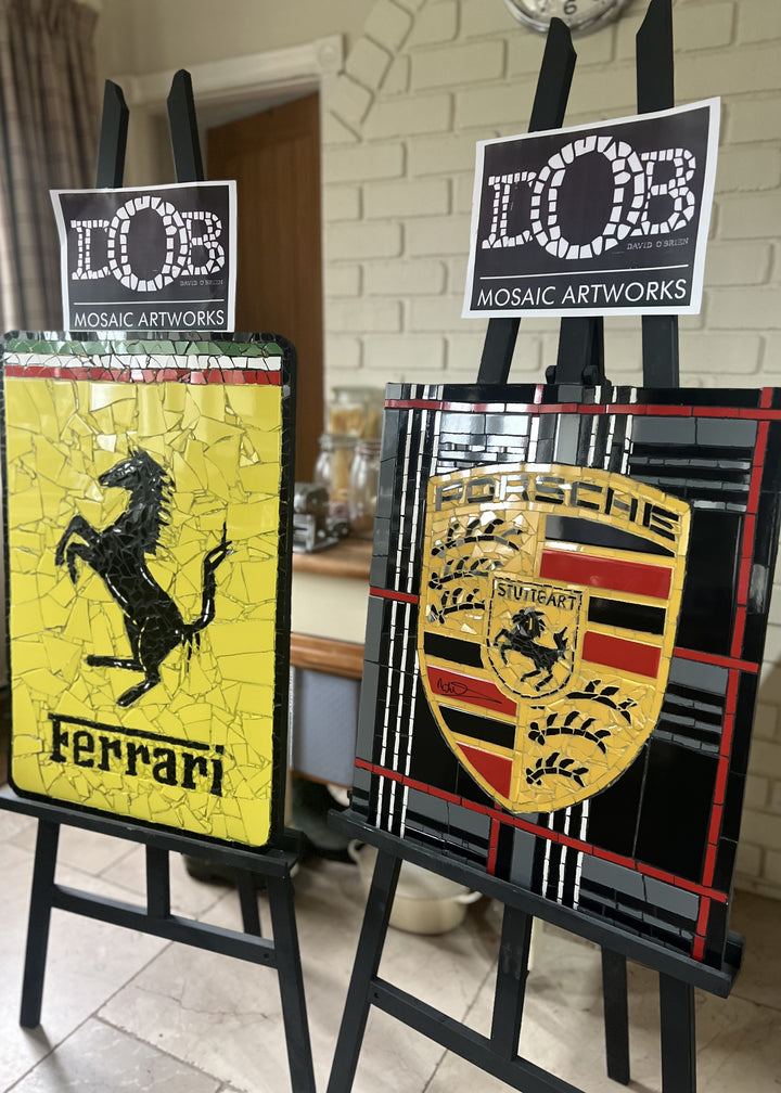 Two handcrafted ceramic mosaic wall artworks featuring Ferrari and Porsche badges, created as bespoke commissions. Each piece is made from hand-cut ceramic tiles in yellow, red, black, white, and grey, celebrating classic motorsport design and automotive heritage through contemporary mosaic craftsmanship.