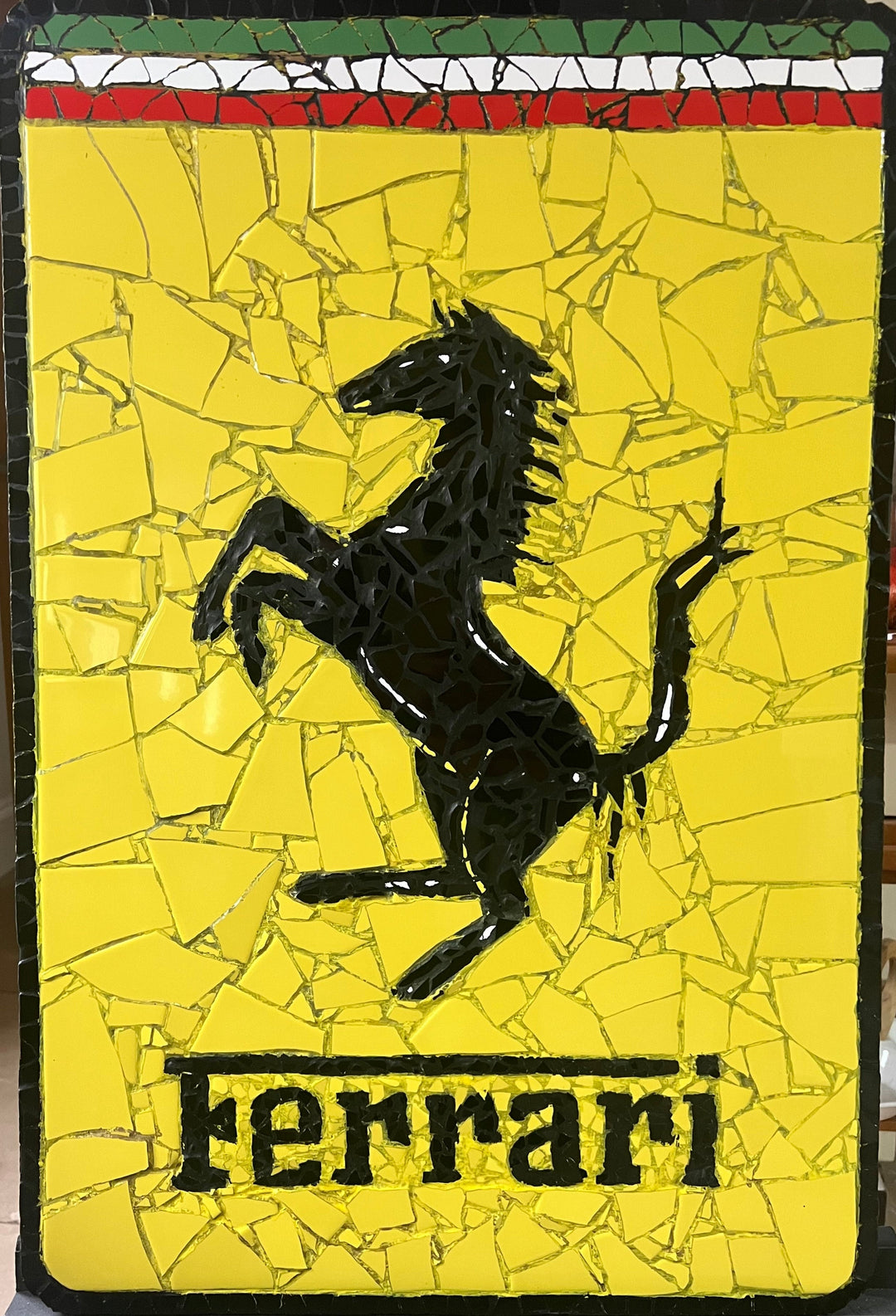 Two handcrafted ceramic mosaic wall artworks featuring Ferrari and Porsche badges, created as bespoke commissions. Each piece is made from hand-cut ceramic tiles in yellow, red, black, white, and grey, celebrating classic motorsport design and automotive heritage through contemporary mosaic craftsmanship.