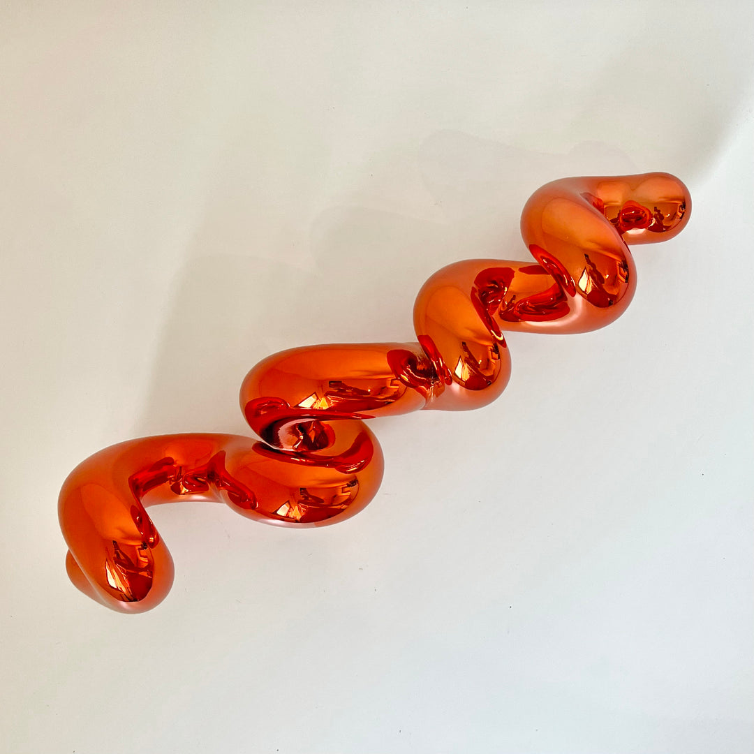 Freestanding sculptural artwork spelling ‘LOVE’ in a flowing, cursive form, finished in high-gloss orange-tinted stainless steel.