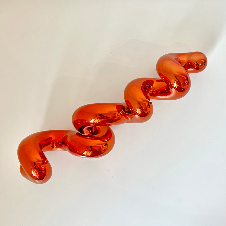 Freestanding sculptural artwork spelling ‘LOVE’ in a flowing, cursive form, finished in high-gloss orange-tinted stainless steel.