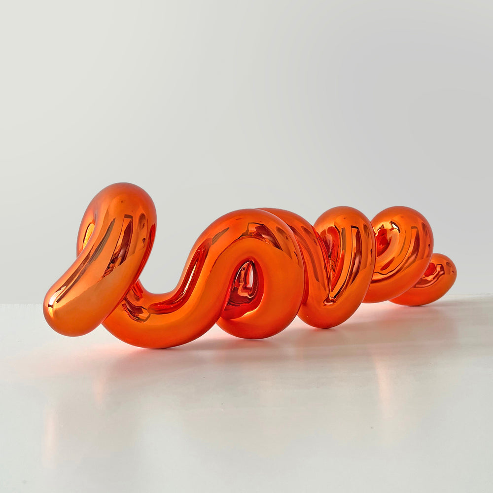 Freestanding sculptural artwork spelling ‘LOVE’ in a flowing, cursive form, finished in high-gloss orange-tinted stainless steel.