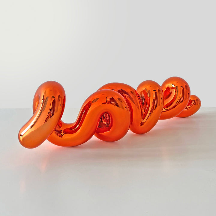 Freestanding sculptural artwork spelling ‘LOVE’ in a flowing, cursive form, finished in high-gloss orange-tinted stainless steel.