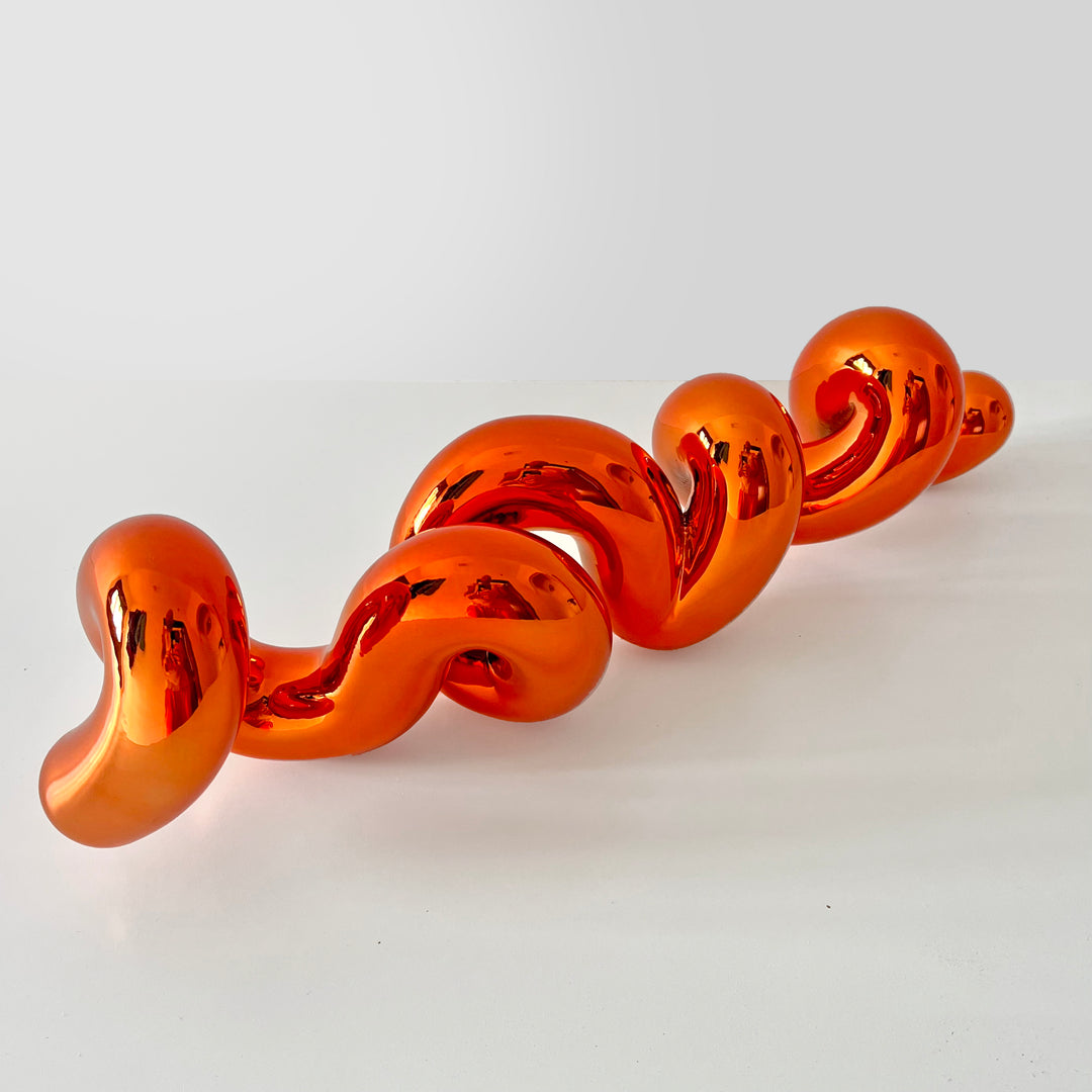 Freestanding sculptural artwork spelling ‘LOVE’ in a flowing, cursive form, finished in high-gloss orange-tinted stainless steel.