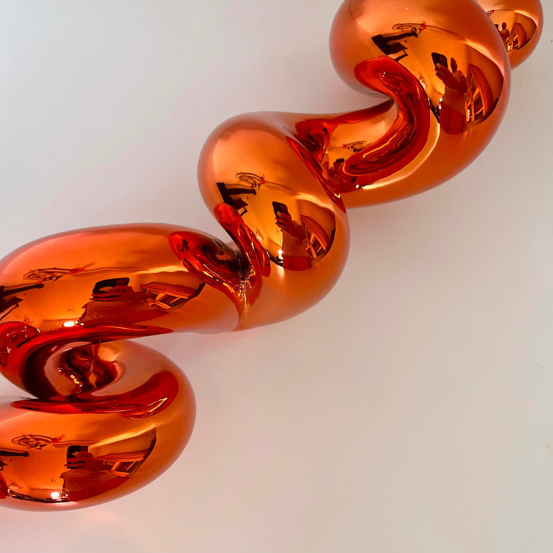 Freestanding sculptural artwork spelling ‘LOVE’ in a flowing, cursive form, finished in high-gloss orange-tinted stainless steel.