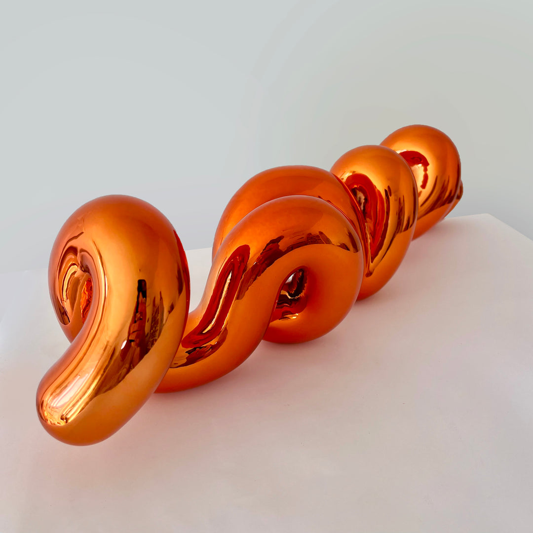 Freestanding sculptural artwork spelling ‘LOVE’ in a flowing, cursive form, finished in high-gloss orange-tinted stainless steel.