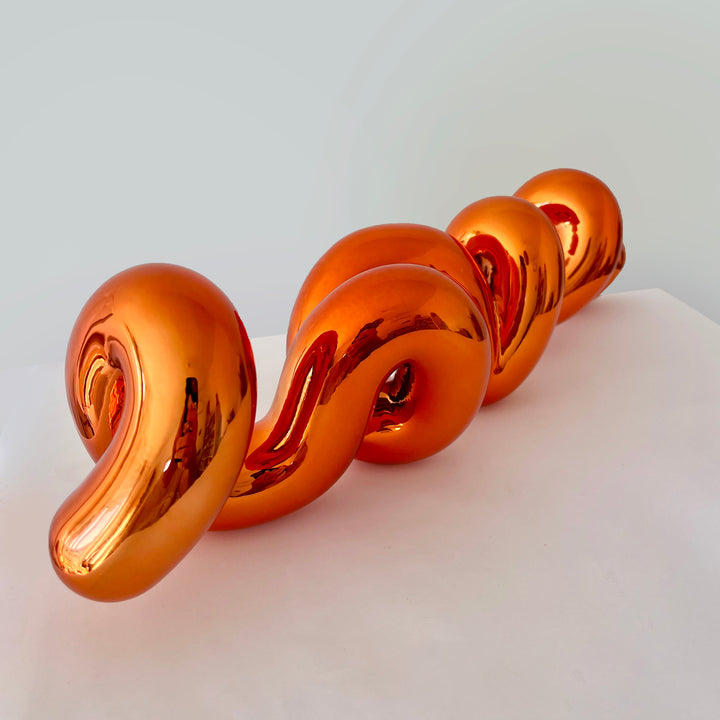 Freestanding sculptural artwork spelling ‘LOVE’ in a flowing, cursive form, finished in high-gloss orange-tinted stainless steel.
