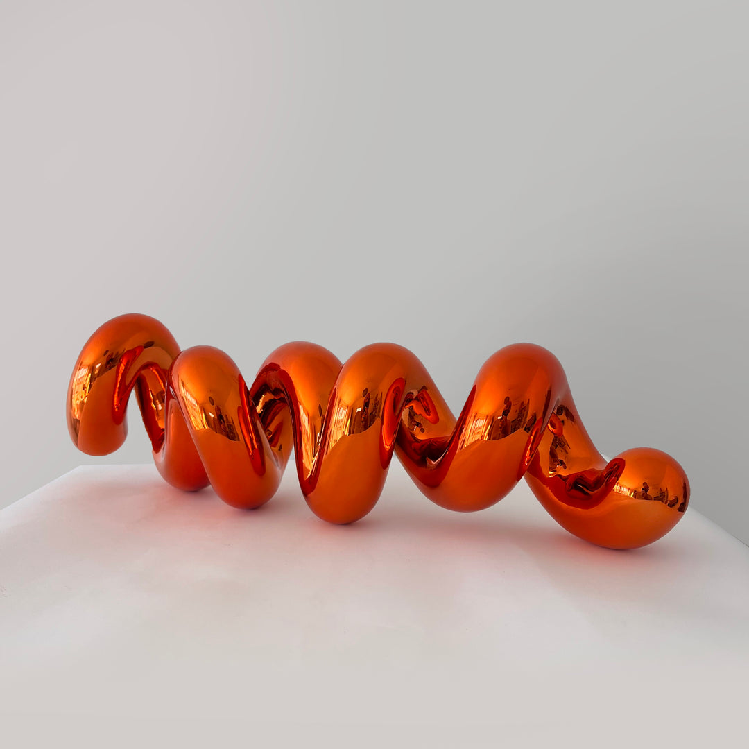 Freestanding sculptural artwork spelling ‘LOVE’ in a flowing, cursive form, finished in high-gloss orange-tinted stainless steel.