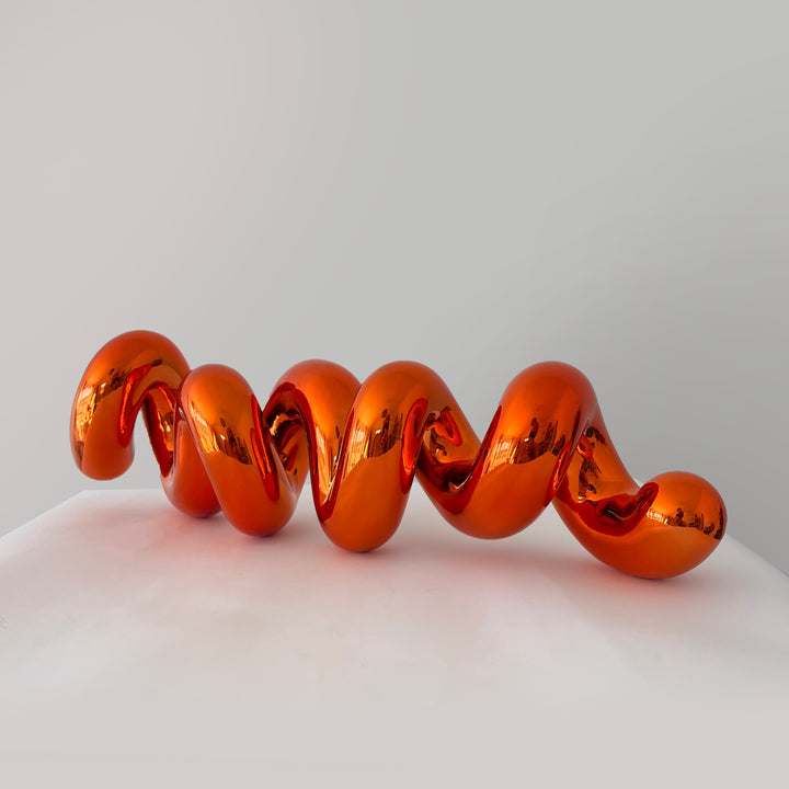 Freestanding sculptural artwork spelling ‘LOVE’ in a flowing, cursive form, finished in high-gloss orange-tinted stainless steel.