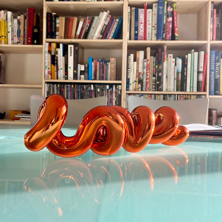 Freestanding sculptural artwork spelling ‘LOVE’ in a flowing, cursive form, finished in high-gloss orange-tinted stainless steel.