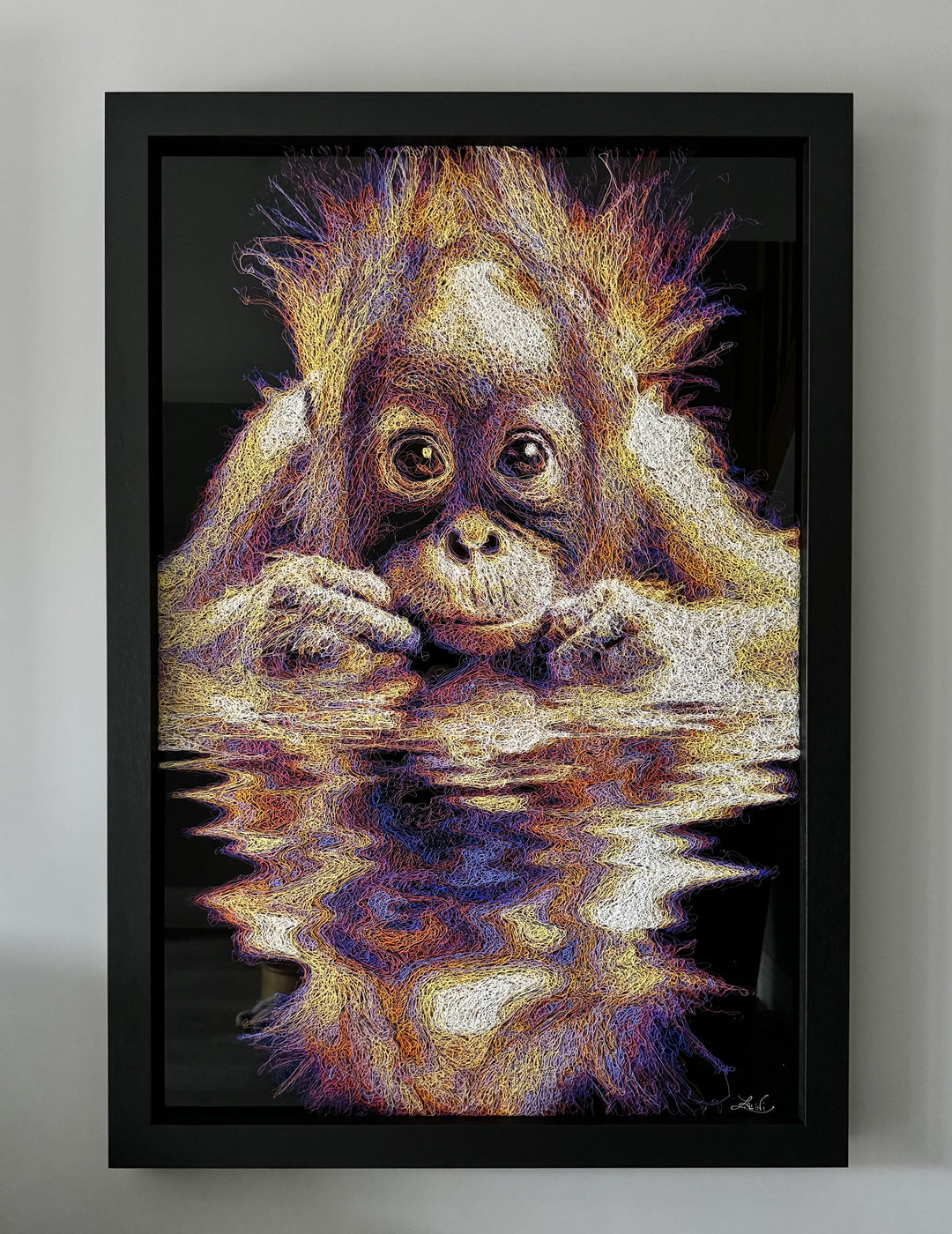 A vibrant textured artwork of a baby orangutan leaning over shimmering water, created with Zalini’s intricate injected-scribble technique, featuring flowing multicoloured lines, bright orange fur, vivid purples and blues, and a mirrored reflection across a glossy black surface.