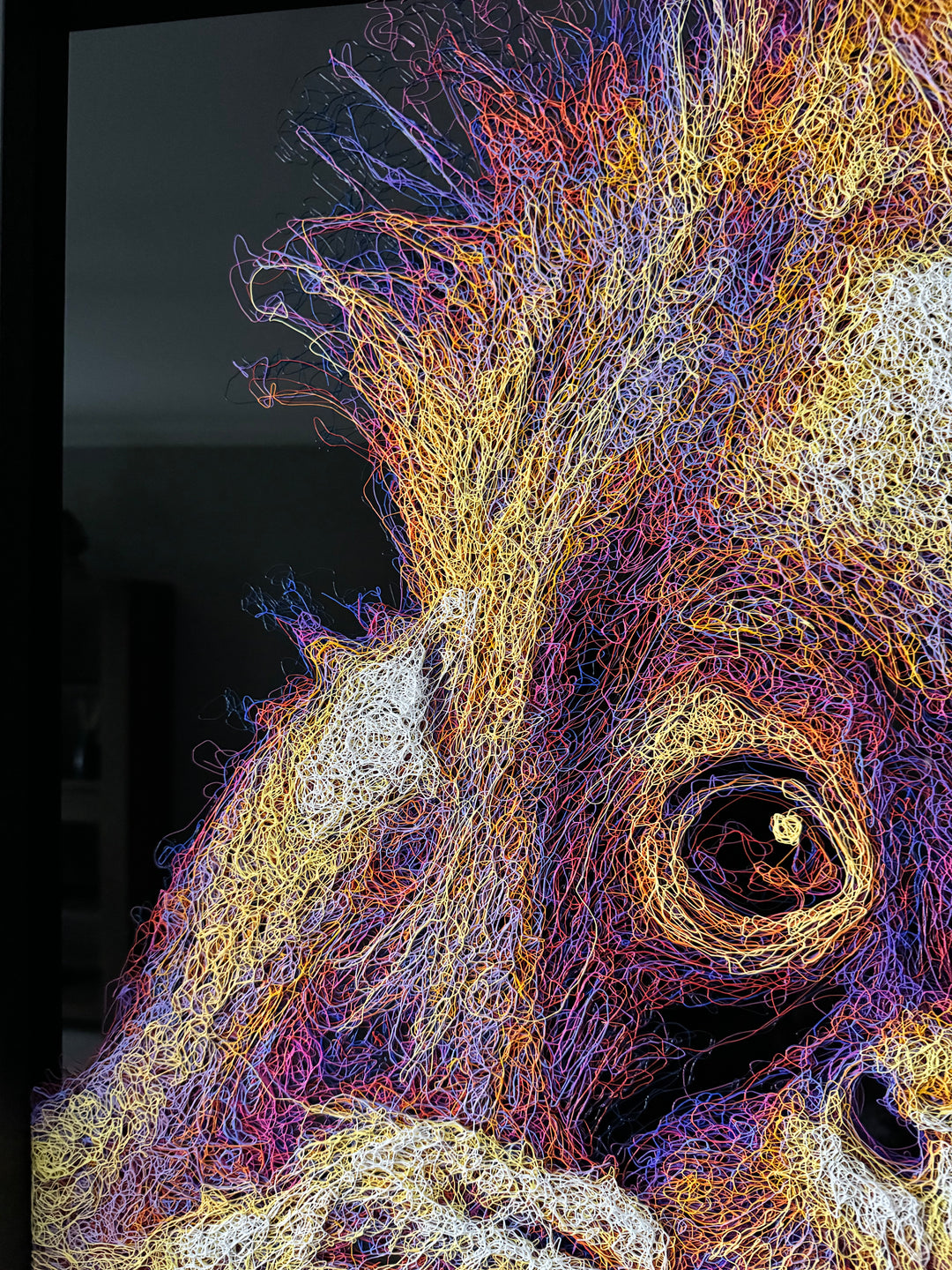 A vibrant textured artwork of a baby orangutan leaning over shimmering water, created with Zalini’s intricate injected-scribble technique, featuring flowing multicoloured lines, bright orange fur, vivid purples and blues, and a mirrored reflection across a glossy black surface.