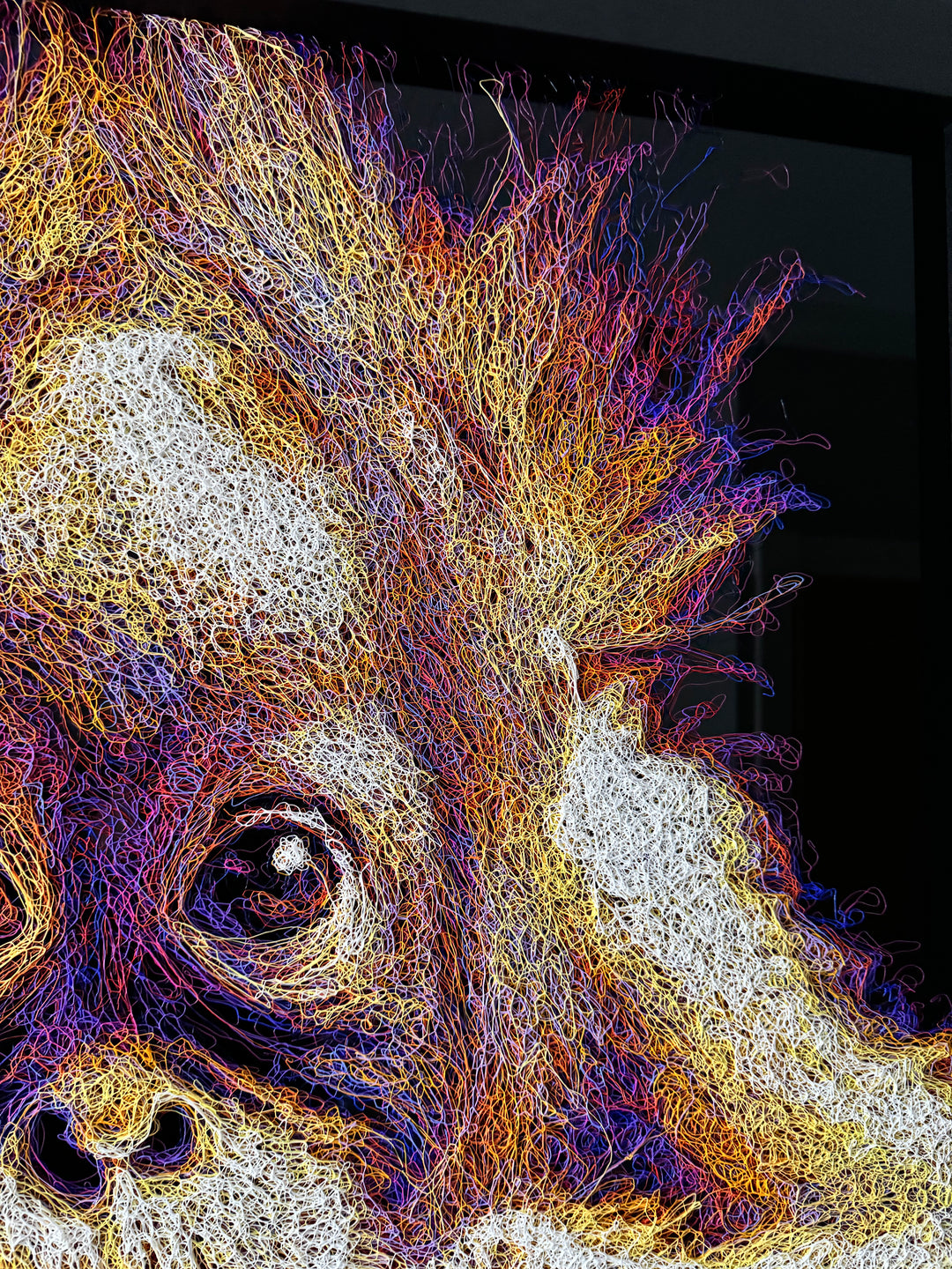 A vibrant textured artwork of a baby orangutan leaning over shimmering water, created with Zalini’s intricate injected-scribble technique, featuring flowing multicoloured lines, bright orange fur, vivid purples and blues, and a mirrored reflection across a glossy black surface.