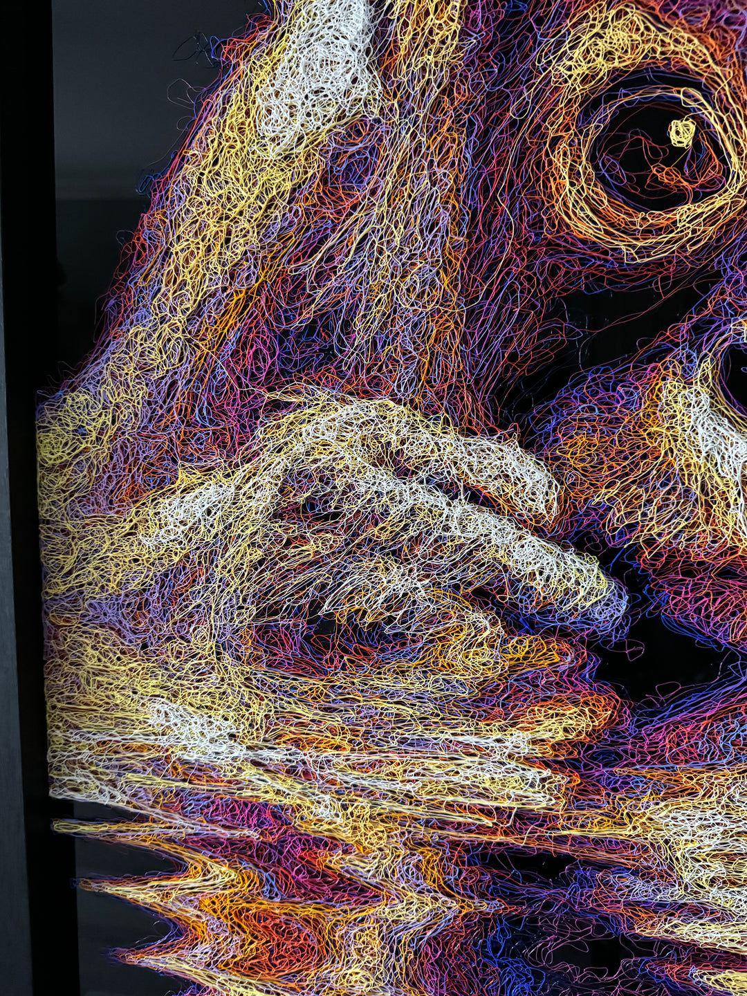 A vibrant textured artwork of a baby orangutan leaning over shimmering water, created with Zalini’s intricate injected-scribble technique, featuring flowing multicoloured lines, bright orange fur, vivid purples and blues, and a mirrored reflection across a glossy black surface.