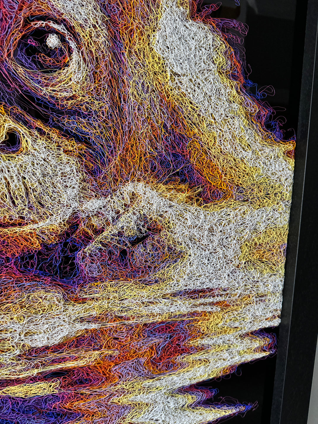 A vibrant textured artwork of a baby orangutan leaning over shimmering water, created with Zalini’s intricate injected-scribble technique, featuring flowing multicoloured lines, bright orange fur, vivid purples and blues, and a mirrored reflection across a glossy black surface.