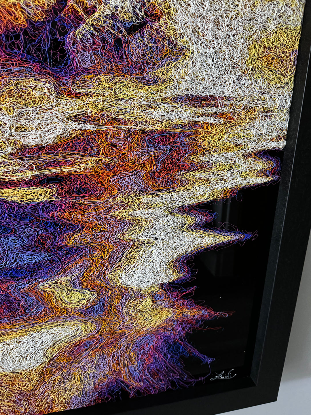 A vibrant textured artwork of a baby orangutan leaning over shimmering water, created with Zalini’s intricate injected-scribble technique, featuring flowing multicoloured lines, bright orange fur, vivid purples and blues, and a mirrored reflection across a glossy black surface.