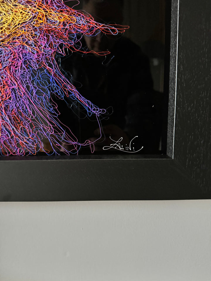 A vibrant textured artwork of a baby orangutan leaning over shimmering water, created with Zalini’s intricate injected-scribble technique, featuring flowing multicoloured lines, bright orange fur, vivid purples and blues, and a mirrored reflection across a glossy black surface.