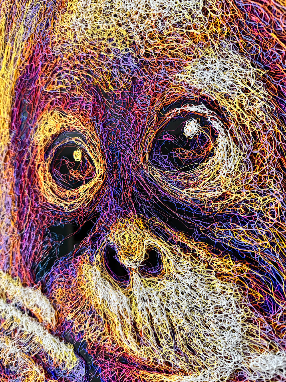 A vibrant textured artwork of a baby orangutan leaning over shimmering water, created with Zalini’s intricate injected-scribble technique, featuring flowing multicoloured lines, bright orange fur, vivid purples and blues, and a mirrored reflection across a glossy black surface.