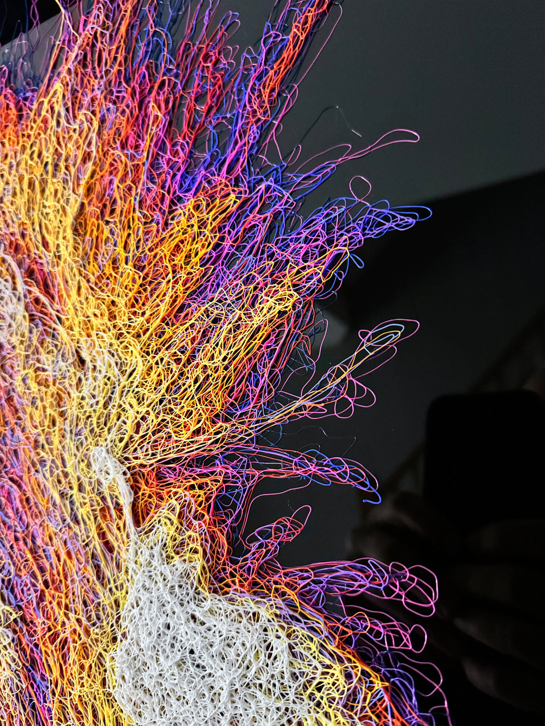 A vibrant textured artwork of a baby orangutan leaning over shimmering water, created with Zalini’s intricate injected-scribble technique, featuring flowing multicoloured lines, bright orange fur, vivid purples and blues, and a mirrored reflection across a glossy black surface.