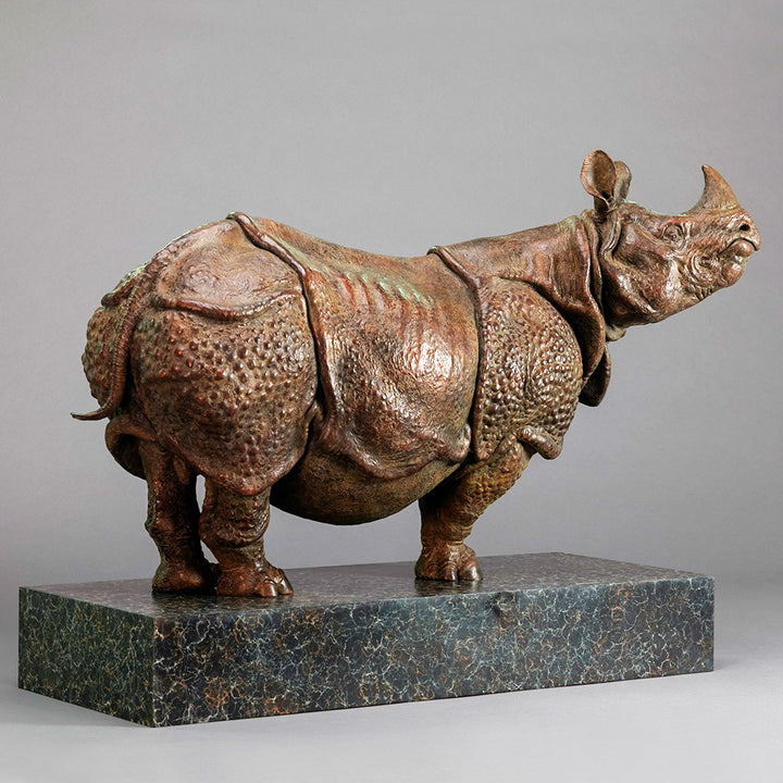 Large bronze Indian rhinoceros sculpture by Nick Bibby, showing armour-like skin folds, textured plates and powerful stance, finished in rich brown patina with subtle green tones on a polished stone plinth.