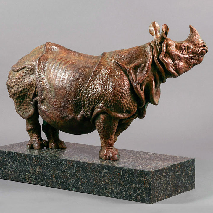 Large bronze Indian rhinoceros sculpture by Nick Bibby, showing armour-like skin folds, textured plates and powerful stance, finished in rich brown patina with subtle green tones on a polished stone plinth.