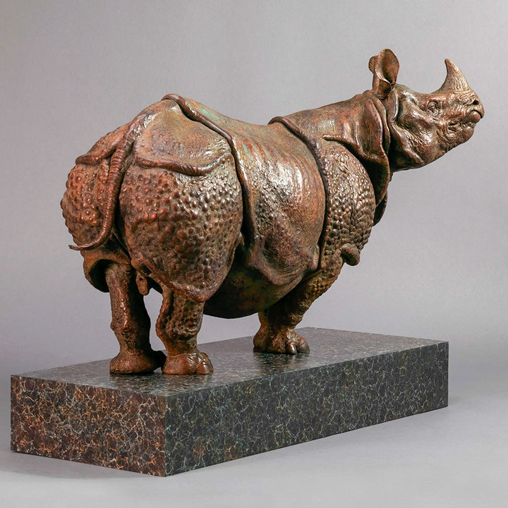 Large bronze Indian rhinoceros sculpture by Nick Bibby, showing armour-like skin folds, textured plates and powerful stance, finished in rich brown patina with subtle green tones on a polished stone plinth.