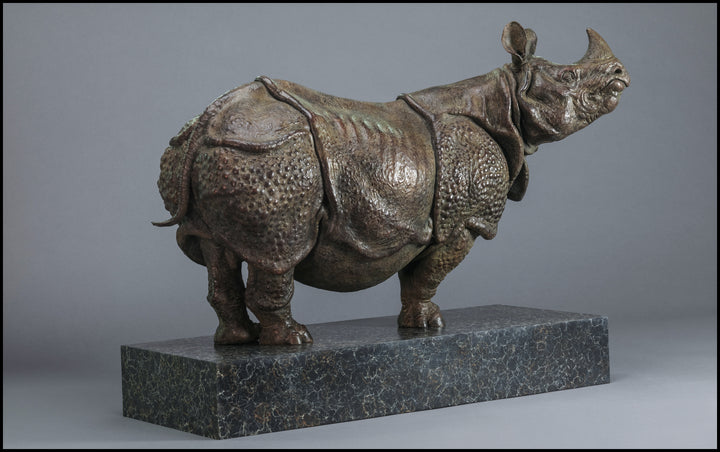 Large bronze Indian rhinoceros sculpture by Nick Bibby, showing armour-like skin folds, textured plates and powerful stance, finished in rich brown patina with subtle green tones on a polished stone plinth.