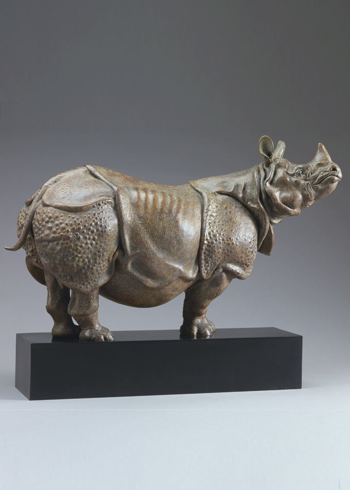 Large bronze Indian rhinoceros sculpture by Nick Bibby, showing armour-like skin folds, textured plates and powerful stance, finished in rich brown patina with subtle green tones on a polished stone plinth.