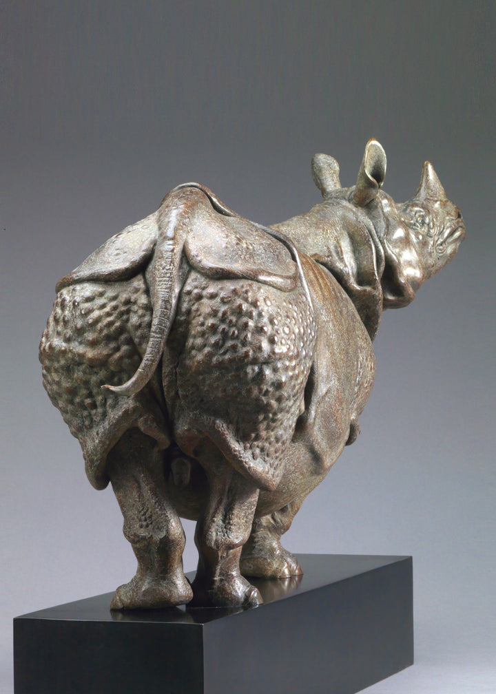 Large bronze Indian rhinoceros sculpture by Nick Bibby, showing armour-like skin folds, textured plates and powerful stance, finished in rich brown patina with subtle green tones on a polished stone plinth.