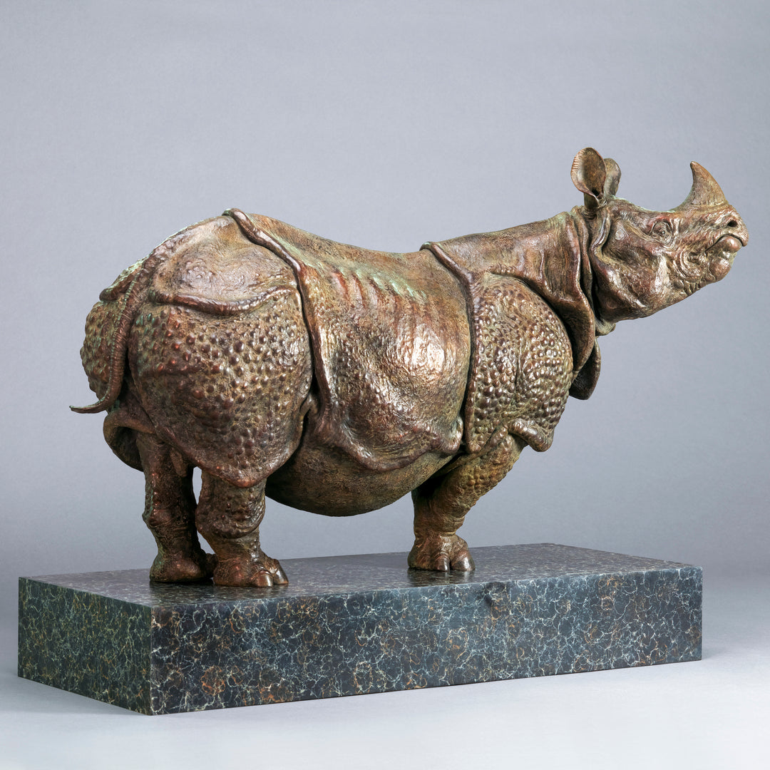 Large bronze Indian rhinoceros sculpture by Nick Bibby, showing armour-like skin folds, textured plates and powerful stance, finished in rich brown patina with subtle green tones on a polished stone plinth.