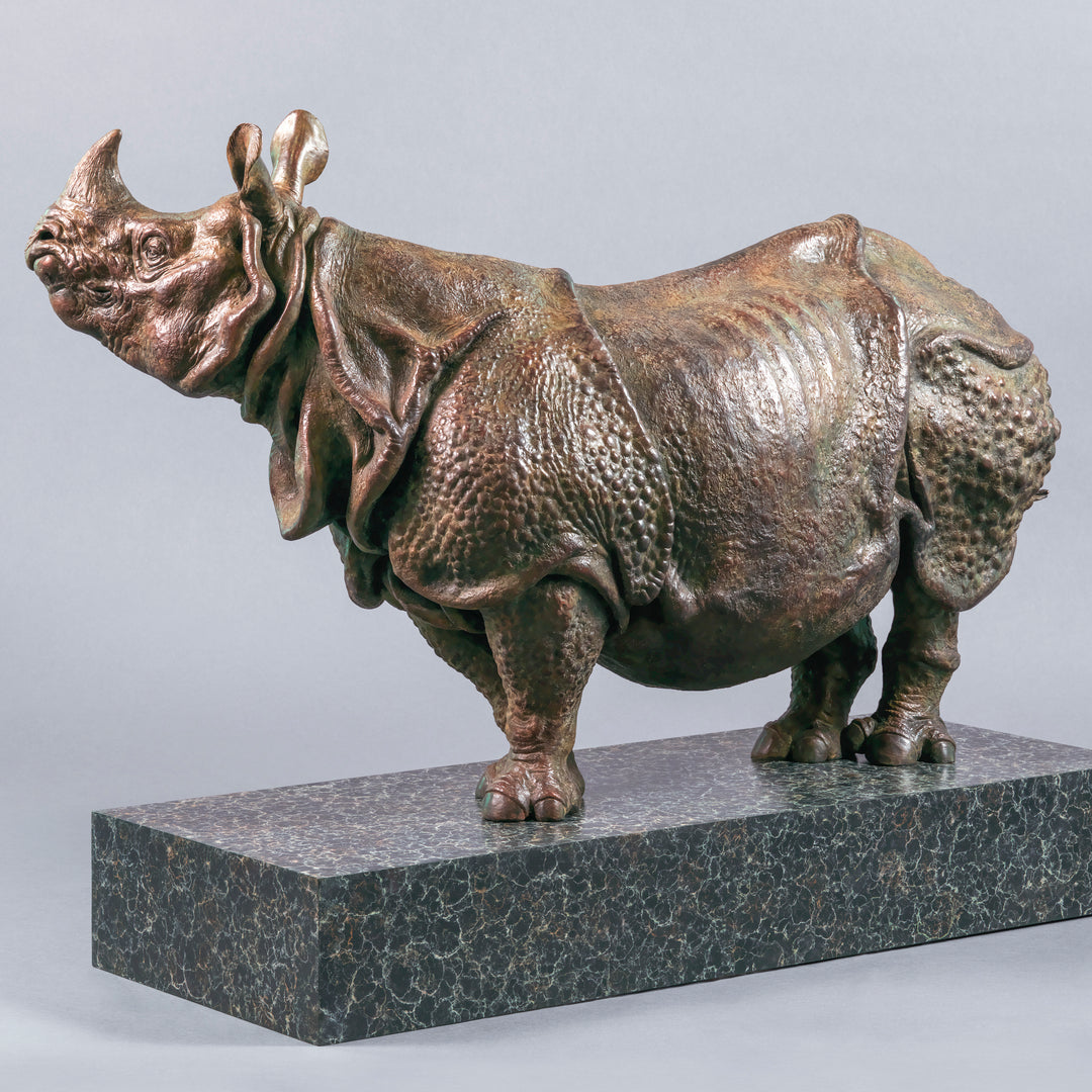 Large bronze Indian rhinoceros sculpture by Nick Bibby, showing armour-like skin folds, textured plates and powerful stance, finished in rich brown patina with subtle green tones on a polished stone plinth.