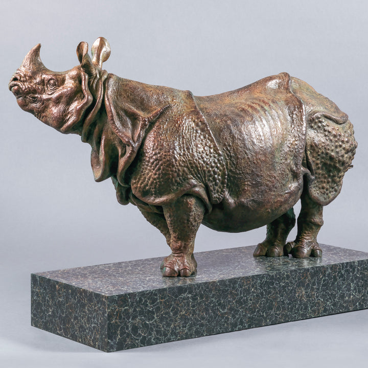 Large bronze Indian rhinoceros sculpture by Nick Bibby, showing armour-like skin folds, textured plates and powerful stance, finished in rich brown patina with subtle green tones on a polished stone plinth.