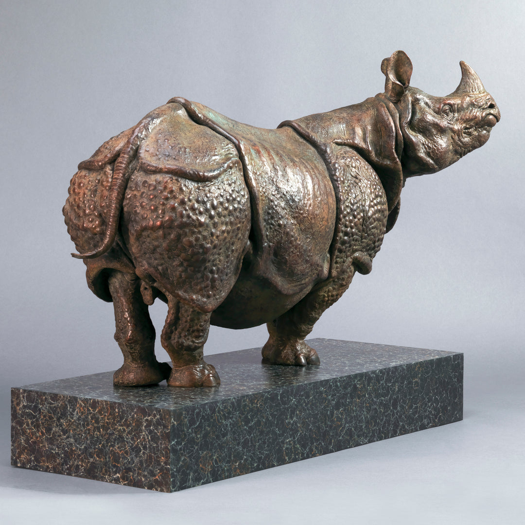 Large bronze Indian rhinoceros sculpture by Nick Bibby, showing armour-like skin folds, textured plates and powerful stance, finished in rich brown patina with subtle green tones on a polished stone plinth.