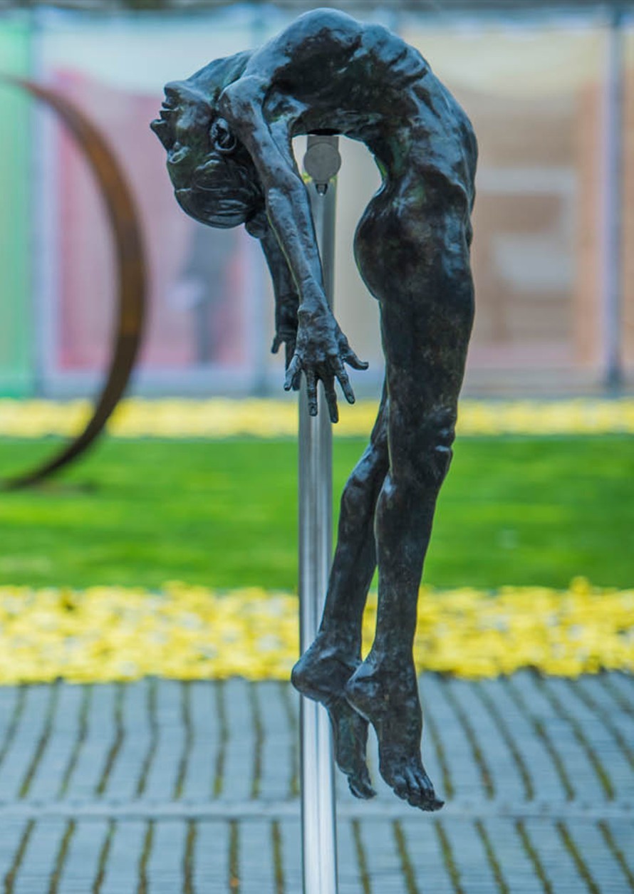 I SPIRIT by Teresa Wells – a monumental one-off bronze sculpture of a nude female figure, arched backwards in a powerful, suspended pose, supported mid-air by a sweeping stainless steel arc anchored to a stone base. Standing 190cm high, the figure’s elongated form captures anatomical detail, strength, and vulnerability, with a dark patinated bronze finish that contrasts against the polished steel support. A contemporary statement of transformation and human resilience.