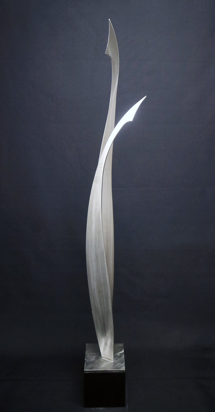 Ian Marlow MRSS stainless steel sculpture Rising Together, featuring two tall, sweeping abstract forms that curve upwards and meet within an elegant contemporary composition, displayed outdoors within a landscaped garden setting.