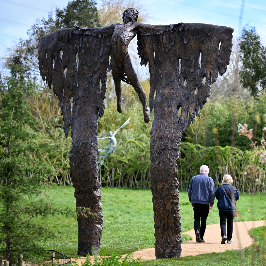 Costruction phases during creation. Monumental bronze sculpture of Icarus mid-flight with expansive feathered wings, captured in an expressive upward pose against a bright sky and lush garden backdrop.
