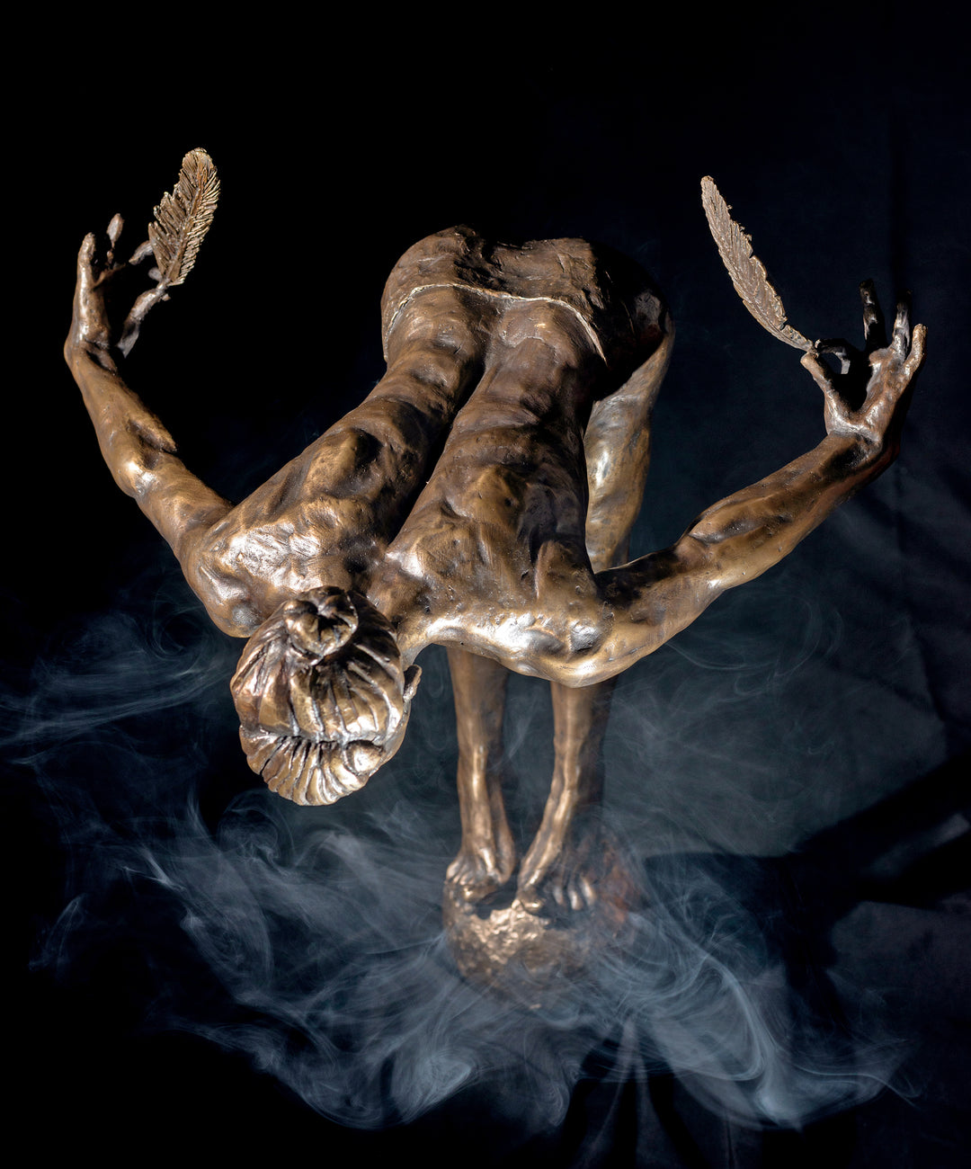 Ingenuity: Often thwarted by the shortsighted by Teresa Wells – a limited-edition bronze and steel sculpture depicting a poised, athletic female figure balanced on tiptoe atop a textured bronze sphere. The figure leans dramatically forward from the hips, arms extended behind and slightly upward, each hand delicately holding a detailed bronze feather. Muscular contours and tendons are rendered with lifelike precision, from the arched spine to the curled toes gripping the sphere. 