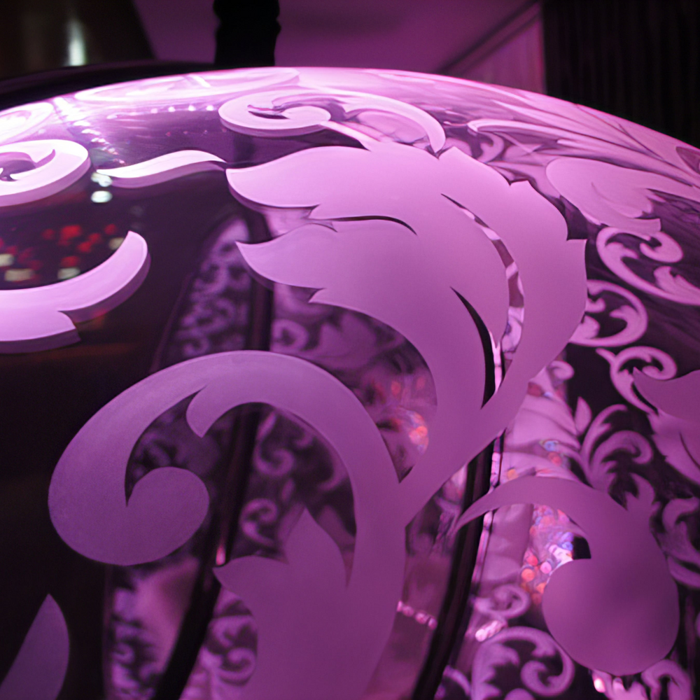 “Illuminated Bubble Chair – Flock Pattern” by Ben Rousseau – a glowing hanging chair crafted from stainless steel, engraved acrylic, and RGB LED light. The spherical design emits soft pink and violet tones, lined with a Mongolian sheepskin cushion.

