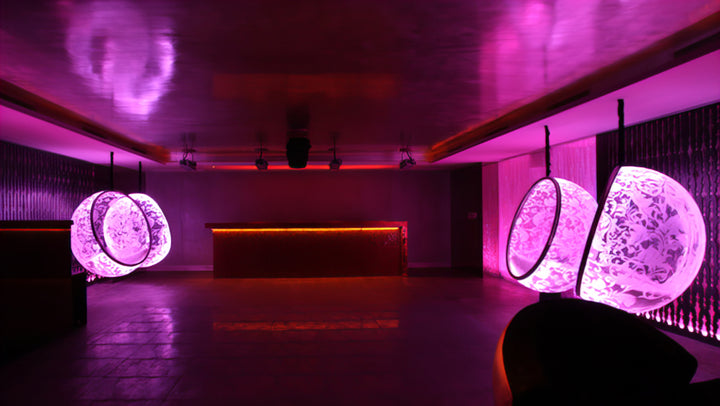 “Illuminated Bubble Chair – Flock Pattern” by Ben Rousseau – a glowing hanging chair crafted from stainless steel, engraved acrylic, and RGB LED light. The spherical design emits soft pink and violet tones, lined with a Mongolian sheepskin cushion.

