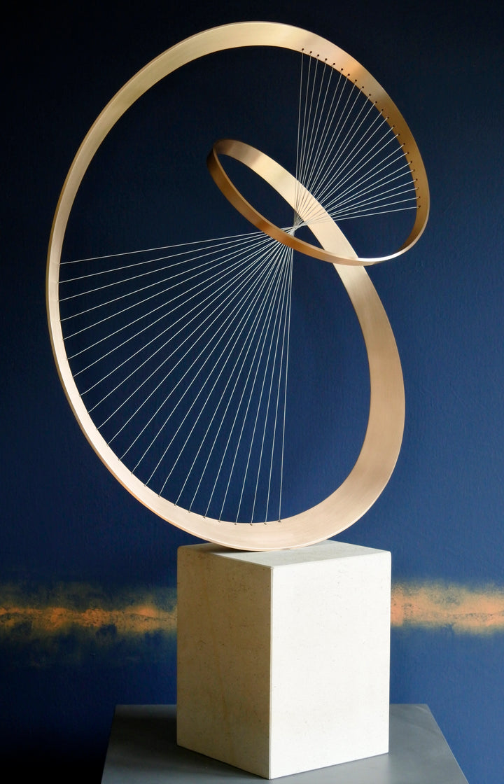 Fabricated bronze sculpture titled Infinity by Thomas Joynes, mounted on a Portland stone plinth. The work features two intersecting bronze curves connected by fine stainless steel micro wires, forming a minimal yet elegant spatial tension. The clean, modernist structure appears weightless and musical, its elliptical ribbons casting delicate linear shadows, evoking motion and balance. Photographed against a deep blue backdrop.