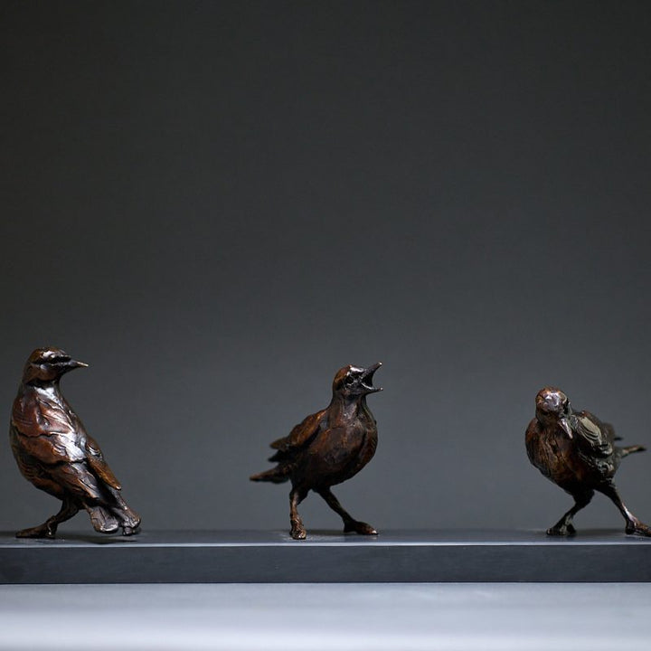 Jane Shaw Community Spirit bronze sculpture depicting a group of starlings perched along a ledge, each bird individually posed to suggest interaction, movement and communication. The figures vary subtly in stance - some alert, some mid-song - capturing the character and rhythm of urban bird life, with a naturalistic bronze finish that highlights feather texture and form against an architectural setting.