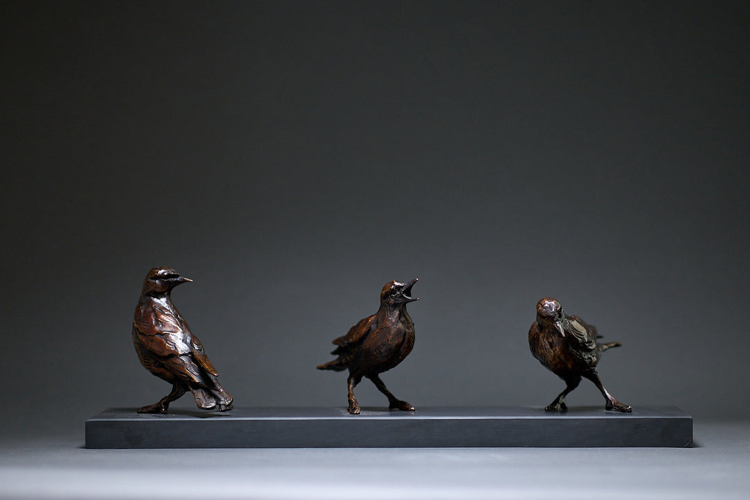 Jane Shaw Community Spirit bronze sculpture depicting a group of starlings perched along a ledge, each bird individually posed to suggest interaction, movement and communication. The figures vary subtly in stance - some alert, some mid-song - capturing the character and rhythm of urban bird life, with a naturalistic bronze finish that highlights feather texture and form against an architectural setting.
