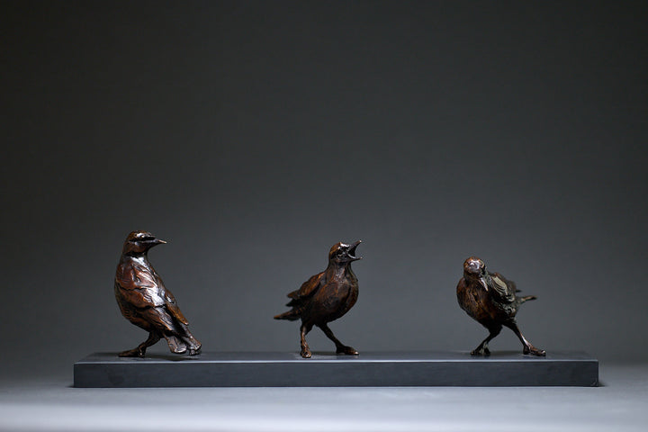 Jane Shaw Community Spirit bronze sculpture depicting a group of starlings perched along a ledge, each bird individually posed to suggest interaction, movement and communication. The figures vary subtly in stance - some alert, some mid-song - capturing the character and rhythm of urban bird life, with a naturalistic bronze finish that highlights feather texture and form against an architectural setting.