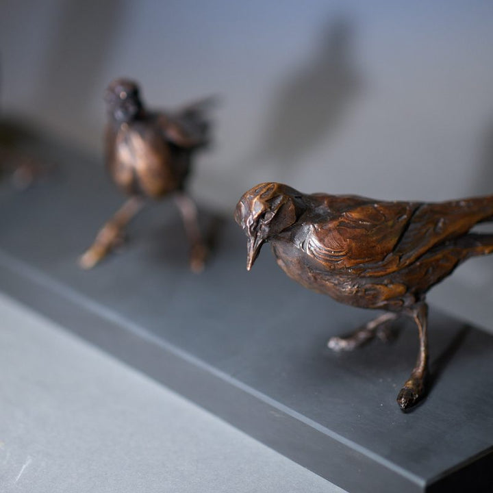 Jane Shaw Community Spirit bronze sculpture depicting a group of starlings perched along a ledge, each bird individually posed to suggest interaction, movement and communication. The figures vary subtly in stance - some alert, some mid-song - capturing the character and rhythm of urban bird life, with a naturalistic bronze finish that highlights feather texture and form against an architectural setting.