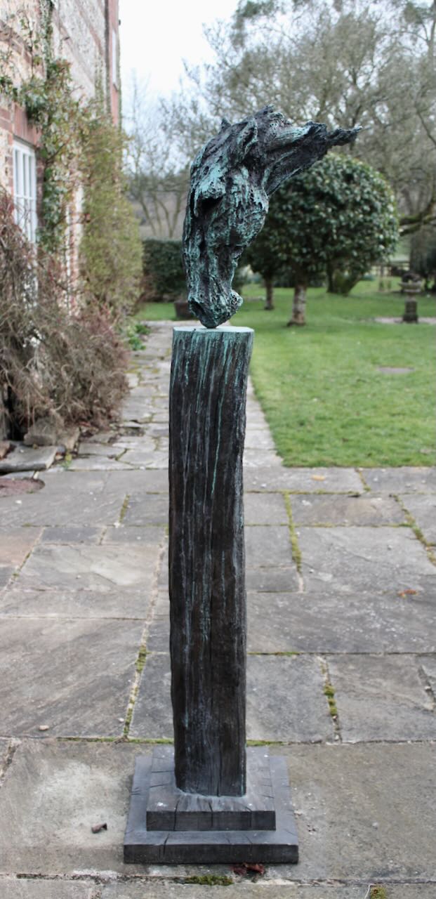 Abstract bronze sculpture of a horse’s head, mounted on a tall corten steel plinth, displayed in various garden and outdoor settings. The textured verdigris patina highlights the expressive contours and emotional form of the equine subject.