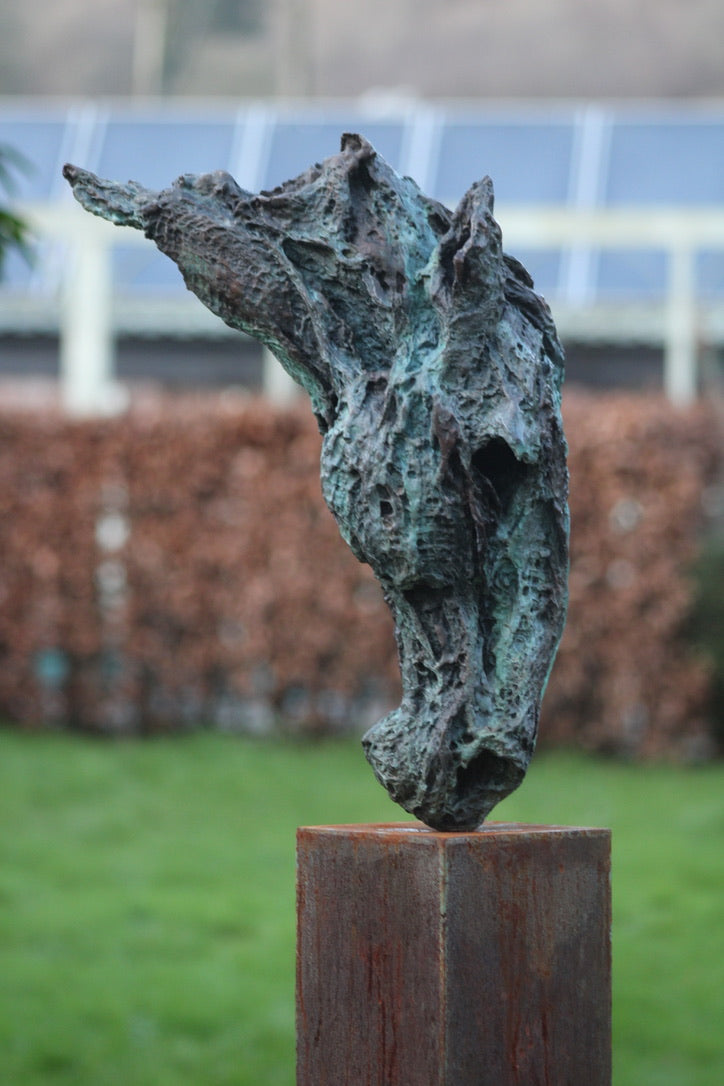 Abstract bronze sculpture of a horse’s head, mounted on a tall corten steel plinth, displayed in various garden and outdoor settings. The textured verdigris patina highlights the expressive contours and emotional form of the equine subject.